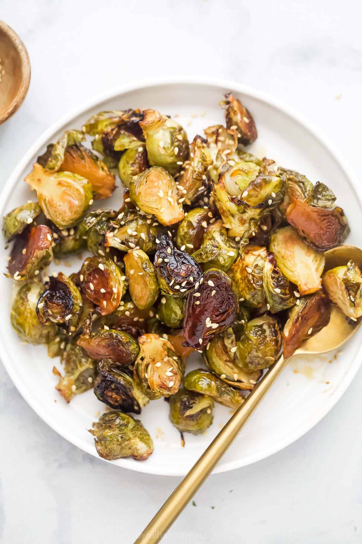 This sweet-and-savory honey roasted Brussels sprouts recipe with fragrant garlic and spicy red pepper flakes is an easy, baked veggie side. Bowl of homemade honey roasted Brussels sprouts with sesame seeds on top.