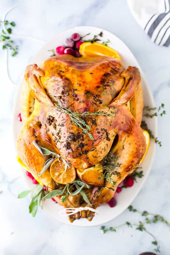 This easy recipe makes the BEST Thanksgiving Turkey! Make moist and juicy roasted turkey. Cooked Thanksgiving turkey on a white platter garnished with cranberries and herbs