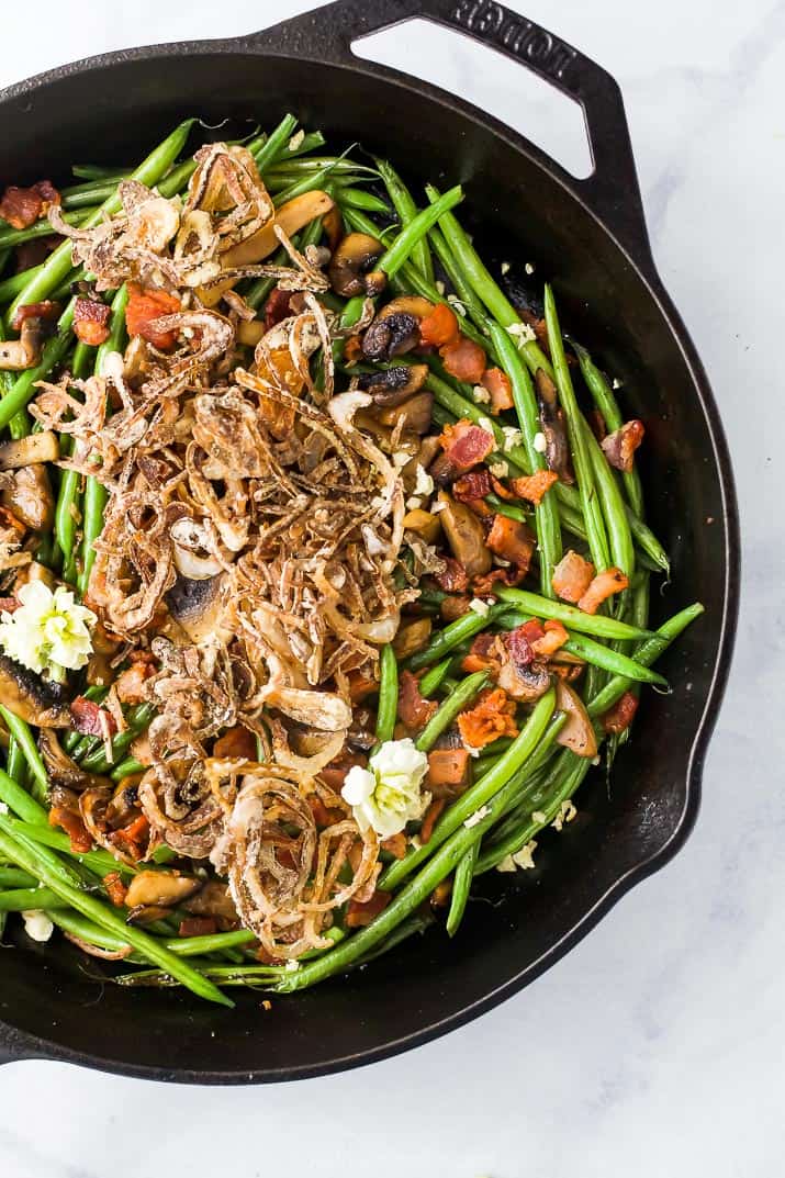 Green bean casserole is made of crunchy sautéed green beans, savory mushrooms, and crispy bacon all topped with homemade fried shallots. Healthy green bean casserole in a skillet.
