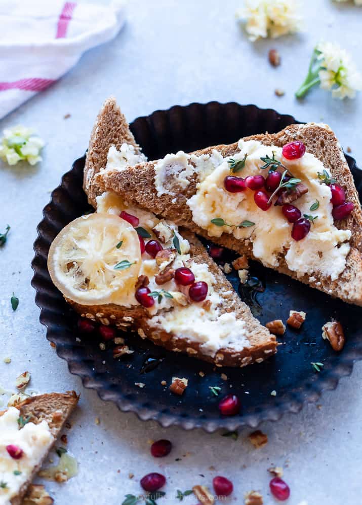 This 5-minute ricotta cheese toast recipe with pomegranate, thyme, candied nuts, and honey is an easy fix for brunch. Sliced ricotta cheese toast with fresh pomegranate, candied pecans, thyme, and honey on top.