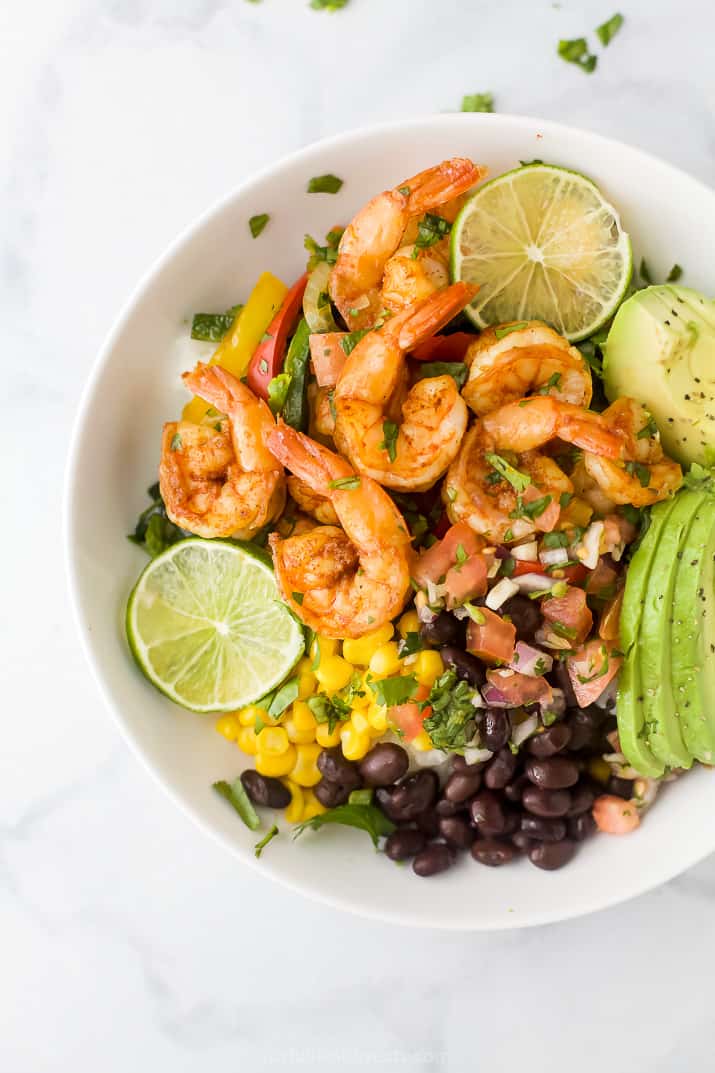 A bowl of shrimp sheet pan fajitas with sliced avocado, black beans, and lime.