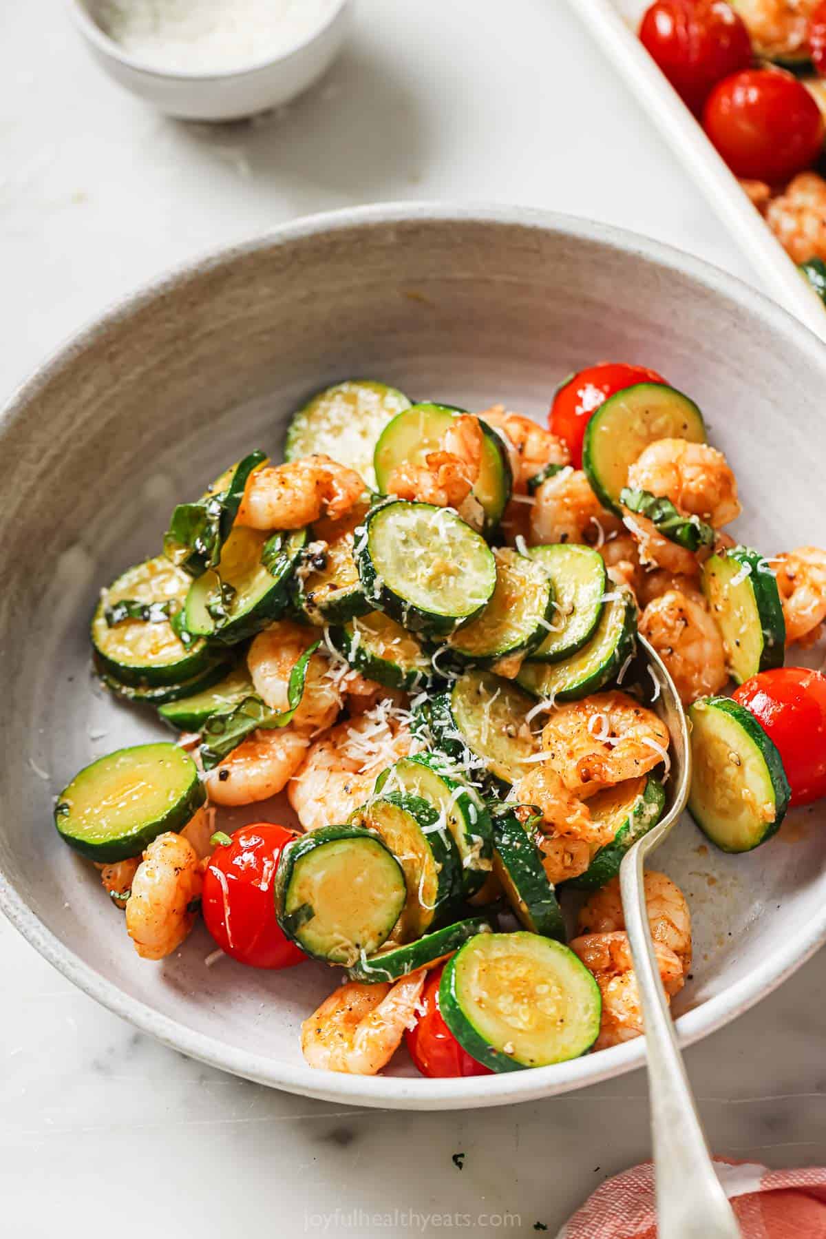 This garlic parmesan sheet pan shrimp recipe is a simple, hearty dinner packed with zucchini, tender squash, and juicy tomatoes. Bowl of sheet pan shrimp with fresh basil as a garnish.