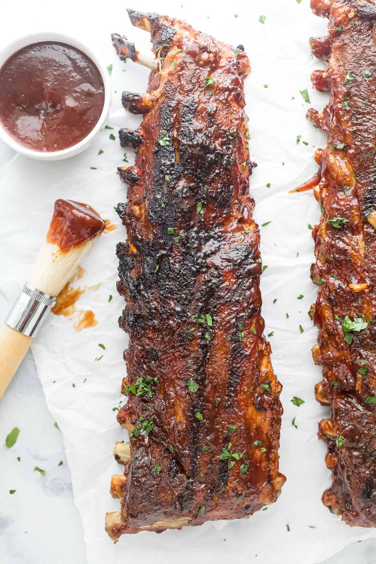 This fall-off-the-bone baby back ribs recipe with garlic-cinnamon spice rub and BBQ glaze will be a juicy, 4th of July favorite. Perfectly charred baby back ribs with more BBQ sauce on the side.