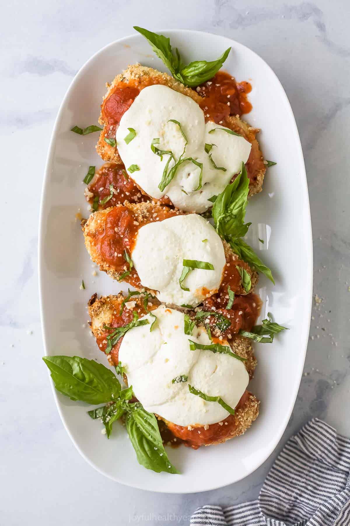 Golden and crunchy, this baked chicken parmesan is a taste of Italy with the help of homemade tomato sauce and fresh mozzarella. Three pieces of baked chicken parmesan on a plate.