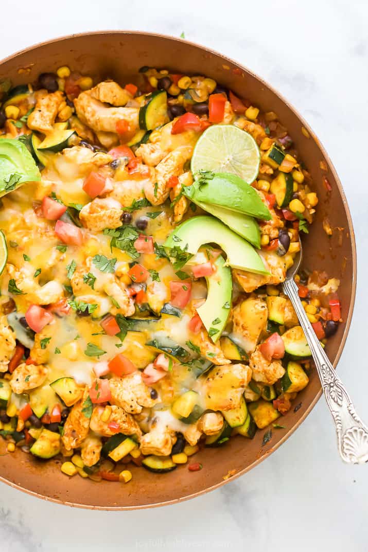Overhead view of a chicken enchilada skillet topped with melted cheese, avocado slices, and lime.