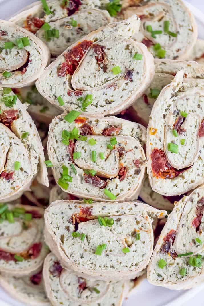 This easy chicken pinwheels recipe is made with pesto, goat cheese, chicken and sun dried tomatoes for an epic bite! the best pesto chicken pinwheel recipe stacked on a platter