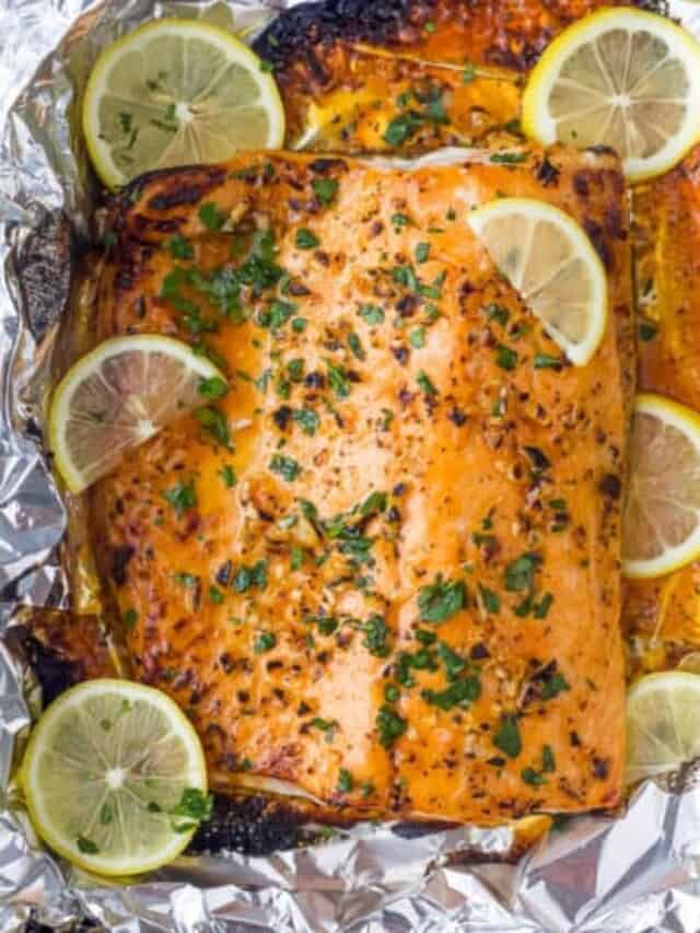 This easy salmon recipe is ready in 20 min! Flaky salmon baked in foil and slathered in a honey garlic butter sauce. One of our fav dinners! overhead photo of garlic butter baked salmon in foil with lemons on top