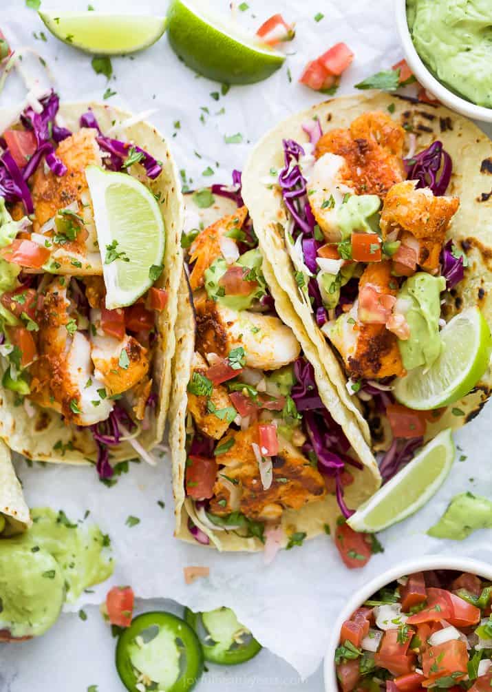 These Baja Fish Tacos are loaded with cabbage slaw, avocado crema and fresh Pico de Gallo. An easy fish taco recipe with no frying needed! overhead photo of epic baja fish tacos with an avocado crema and lime wedges