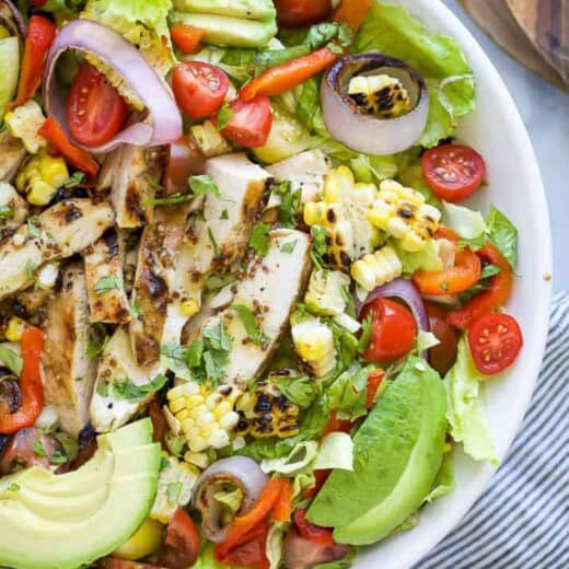 a bowl filled with a grilled honey mustard chicken salad with avocado and veggies