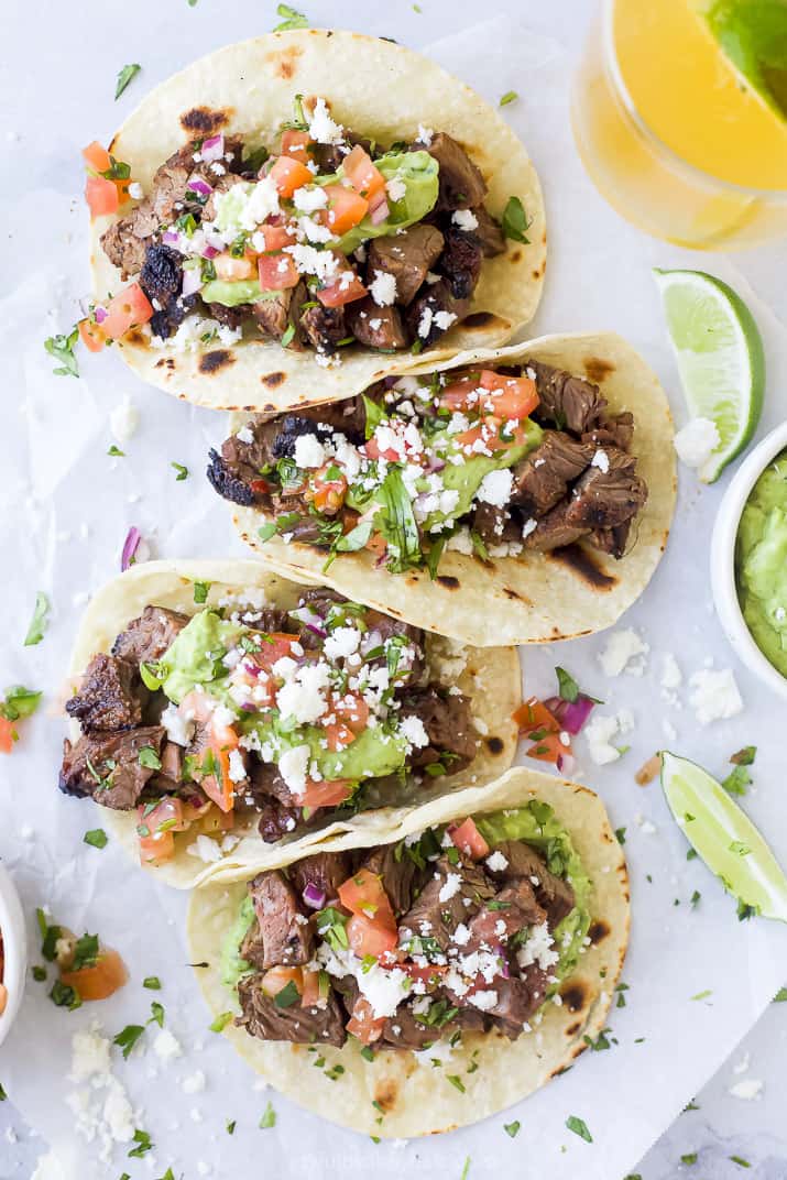 overhead photo of four corn tacos filled with marinated carne asada meat with avocado crema