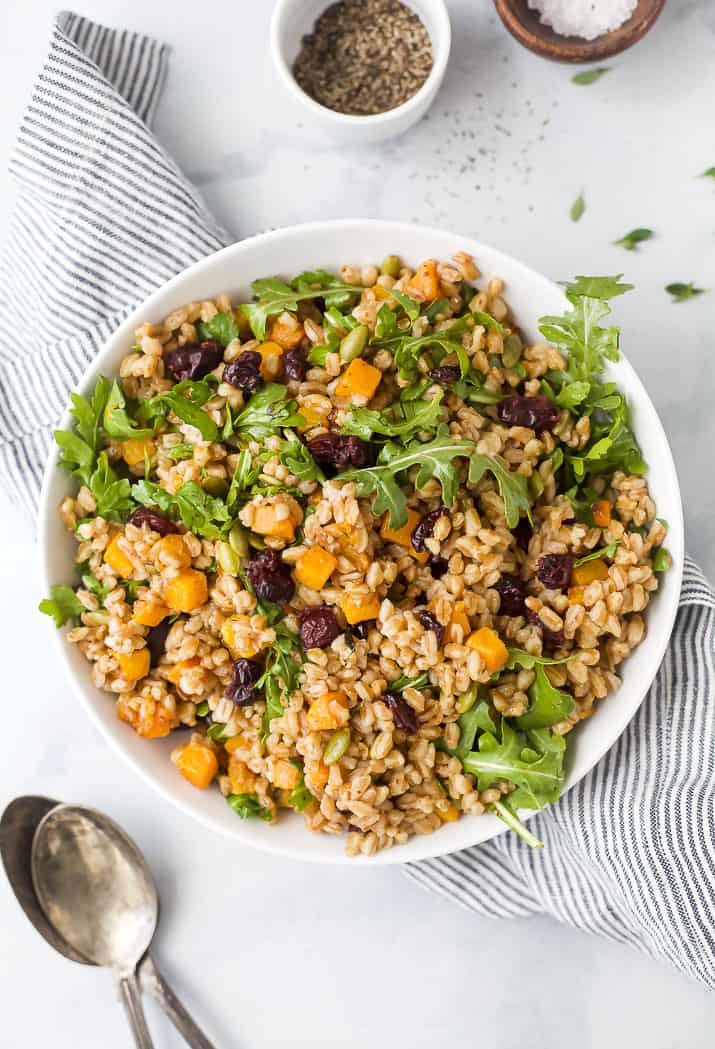A bowl of hearty farro salad with roasted butternut squash, cranberries, arugula, pepitas, and maple-Dijon dressing.