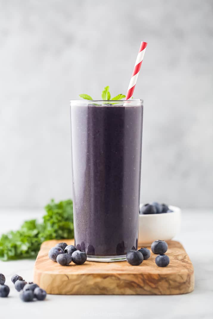High Protein Blueberry Kale Smoothie A Kale Protein Smoothie in a Tall Glass with a Red and White Striped Straw
