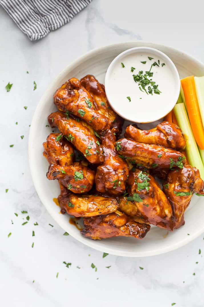 Close up overhead view of air fryer chicken wings on a white plate next to a side of crudités and ranch dressing.