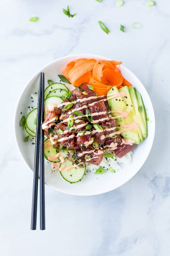 A White Bowl Containing Seasoned Tuna, Veggies, Rice and Sriracha Mayo