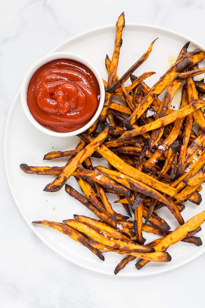 Learn how to make crispy air fryer sweet potato fries in no time! Seasoned with smoked paprika, this easy side dish is a family favorite! Sweet potato fries on a plate with ketchup.
