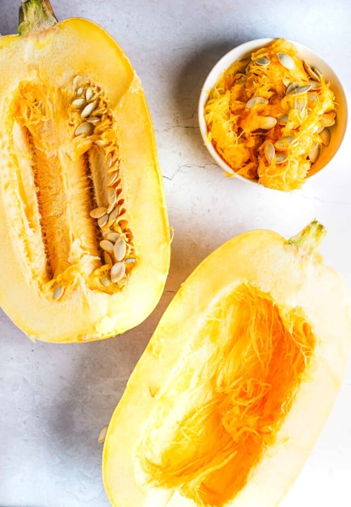 Half a spaghetti squash with all of the seeds scraped out beside the other half with the seeds still inside
