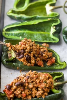Two poblano peppers with the ground turkey filling added beside two empty pepper halves