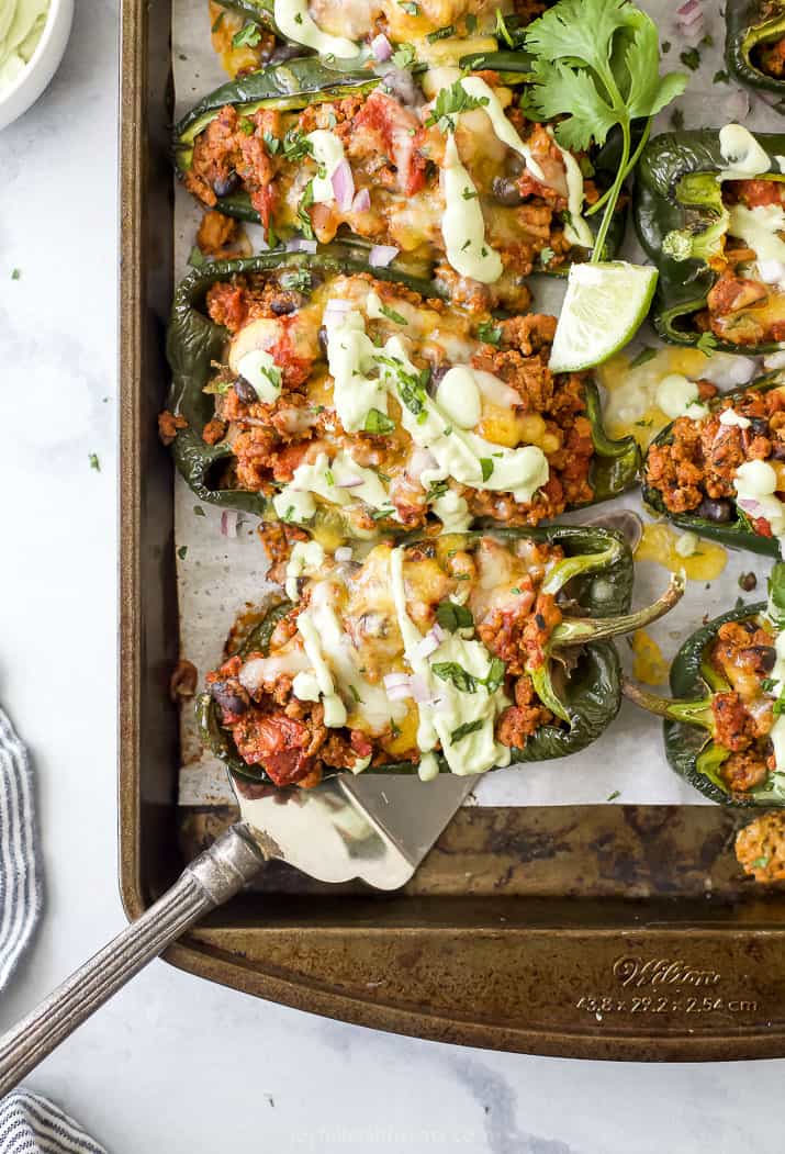 These easy Turkey Stuffed Poblano Peppers are topped with melty cheese and a refreshing avocado crema. You will savor every last bite! A baking sheet full of turkey stuffed poblano peppers topped with avocado crema and chopped cilantro