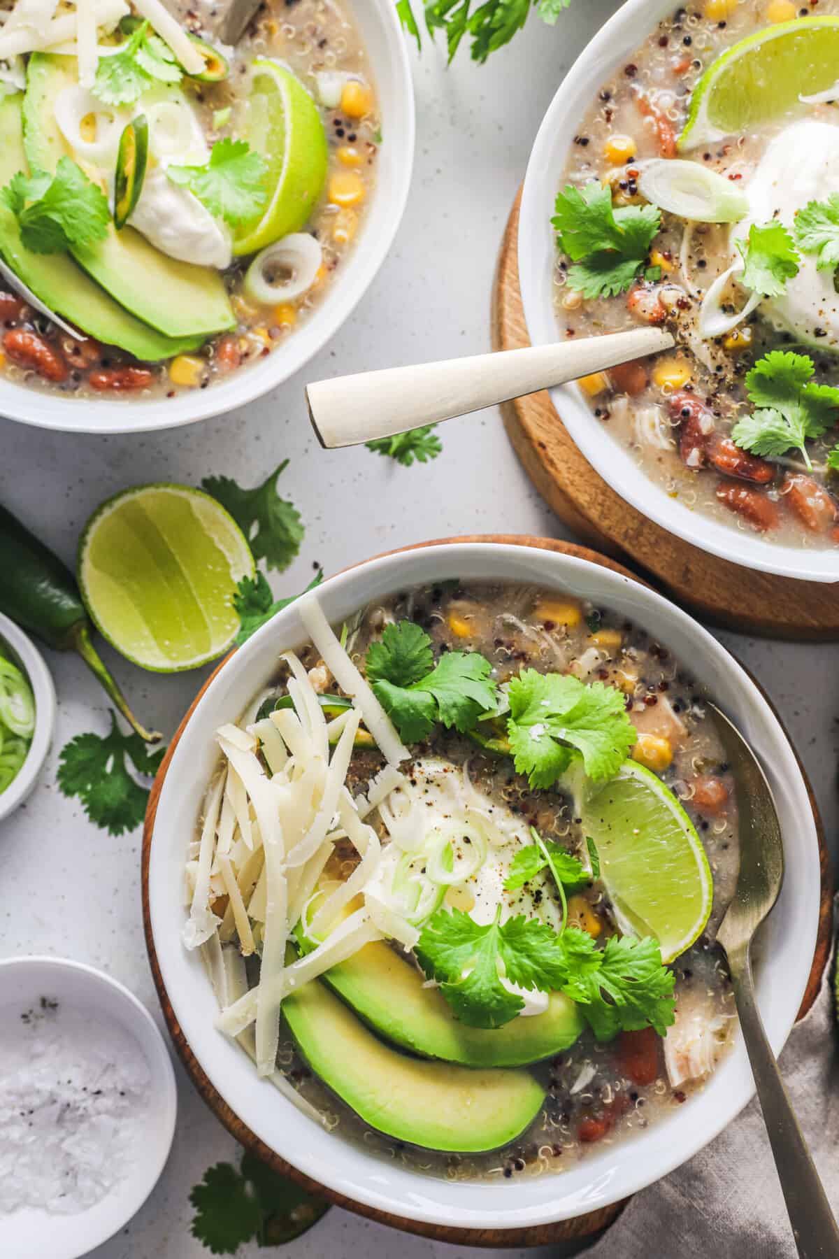 This easy white chicken chili recipe is filled with tender chicken, white beans, and tons of flavor! Just add everything to your crockpot. Three servings of crockpot chicken chili in separate bowls on a white countertop.