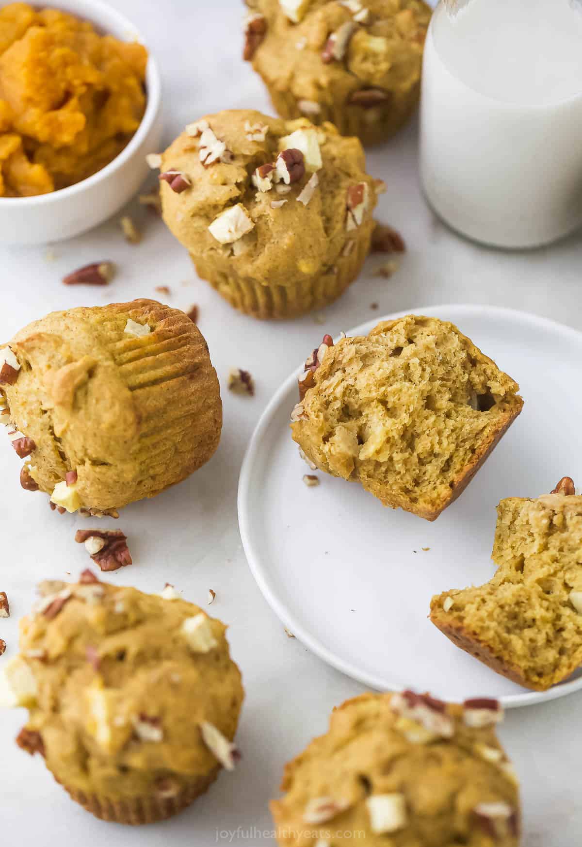 Two halves of an apple muffin on a white plate with more muffins beside it