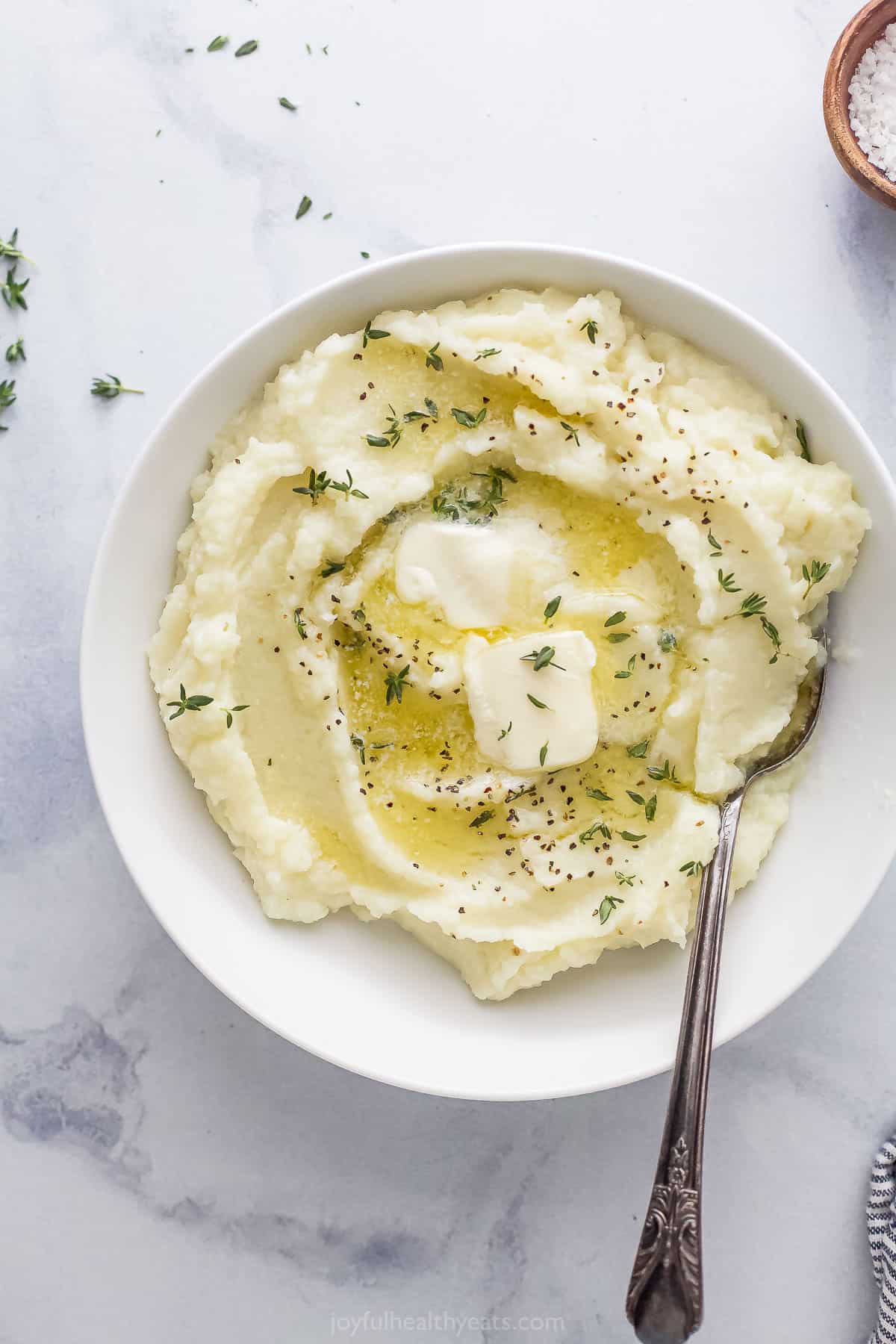 An overhead shot of a bowl of cauliflower puree on top of a black and white marble surface