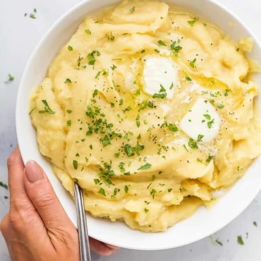 A hand holding a large bowl of parsnip puree topped with butter and chopped parsley