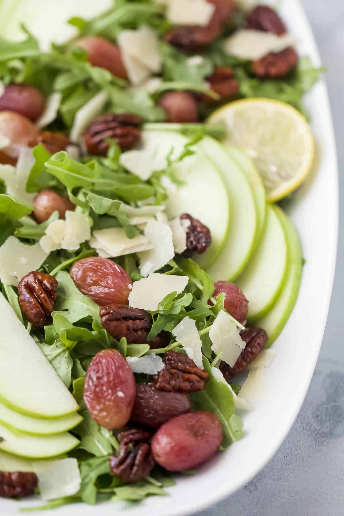 A freshly-made arugula pecan salad in a serving platter with a lemon slice garnish
