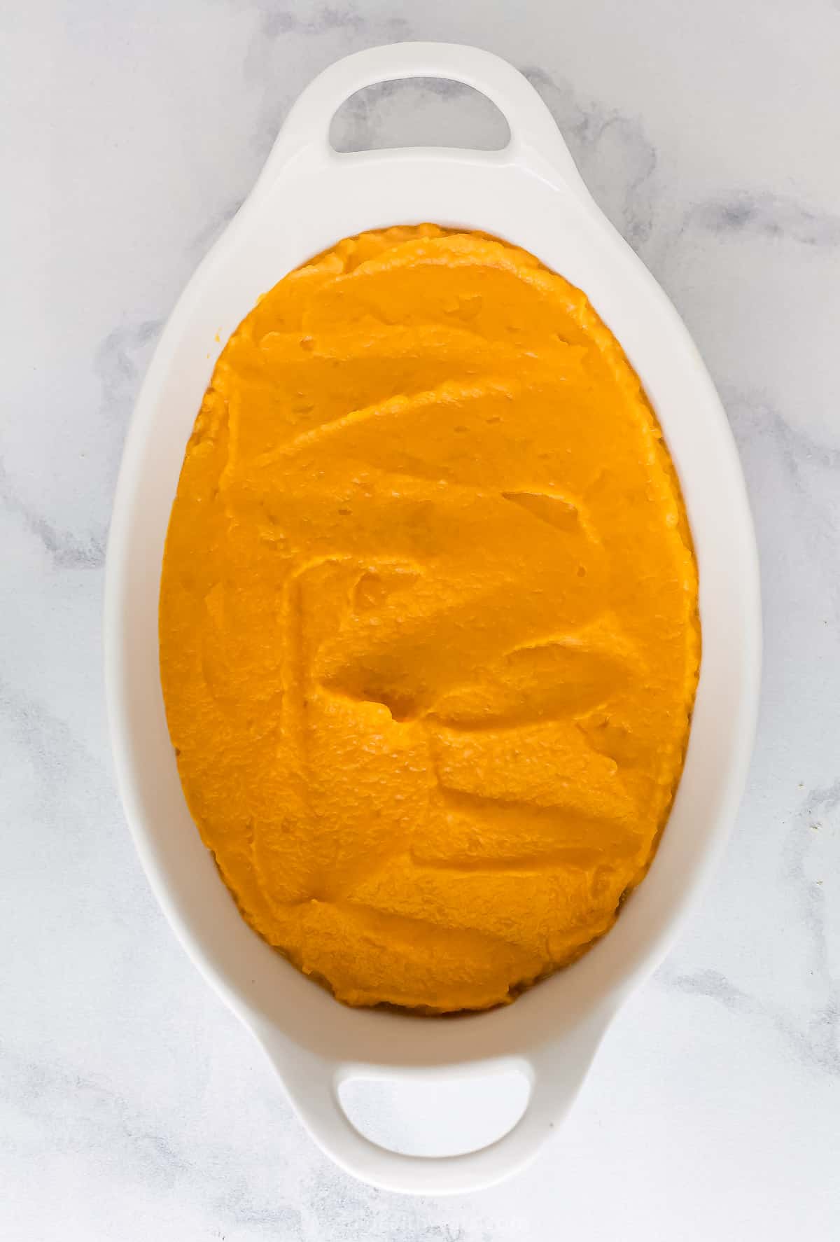 The prepared sweet potato casserole filling spread evenly into a white casserole dish with handles