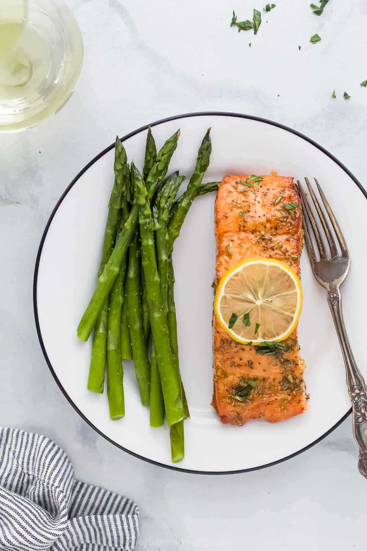 Tender, flaky salmon in 20 minutes? You bet! This easy air fryer salmon recipe makes perfectly cooked salmon with honey garlic sauce. A white plate with air fryer salmon next to a serving of asparagus.