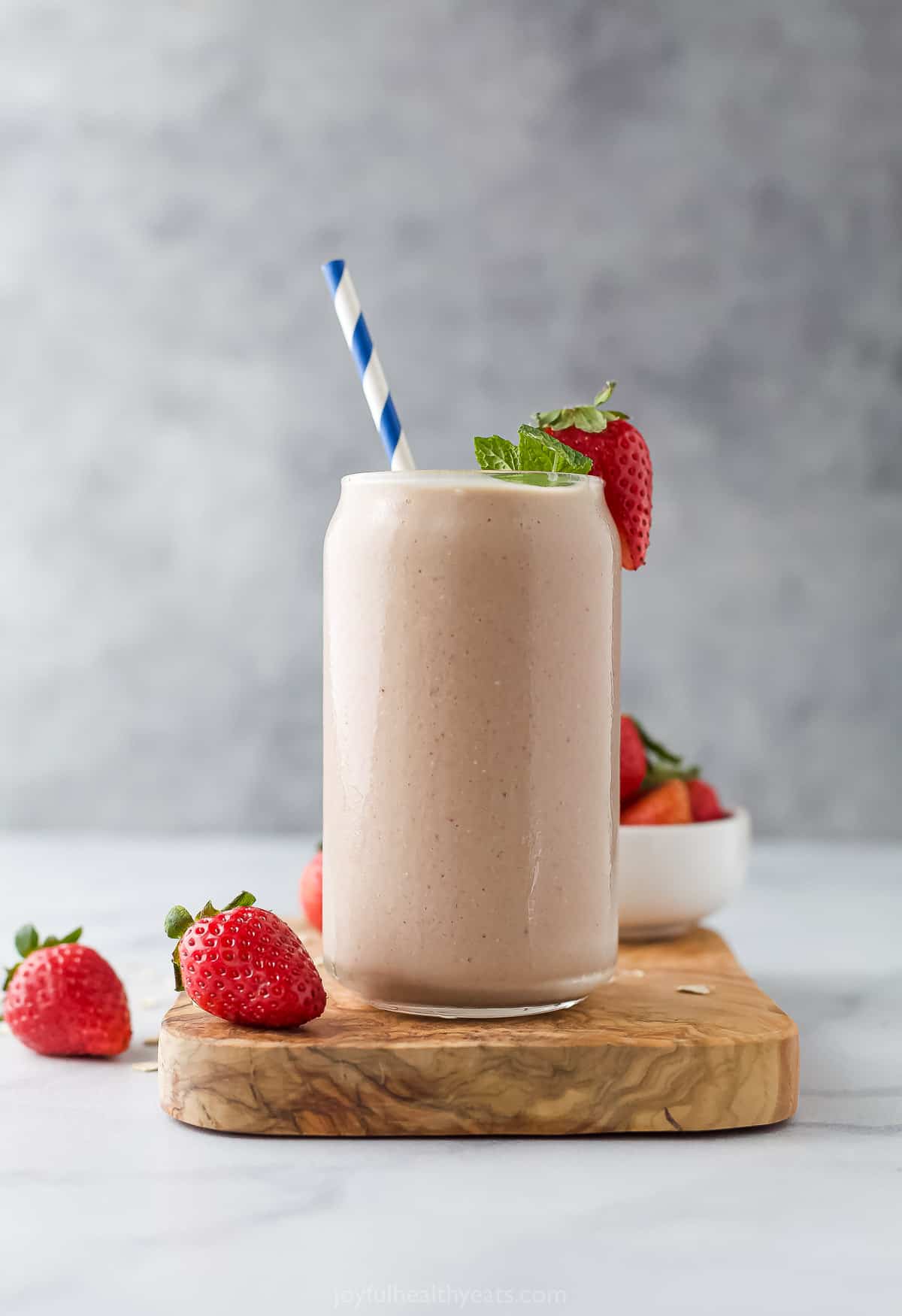 A strawberry banana smoothie in a tall glass on a marble counter beside two fresh strawberries