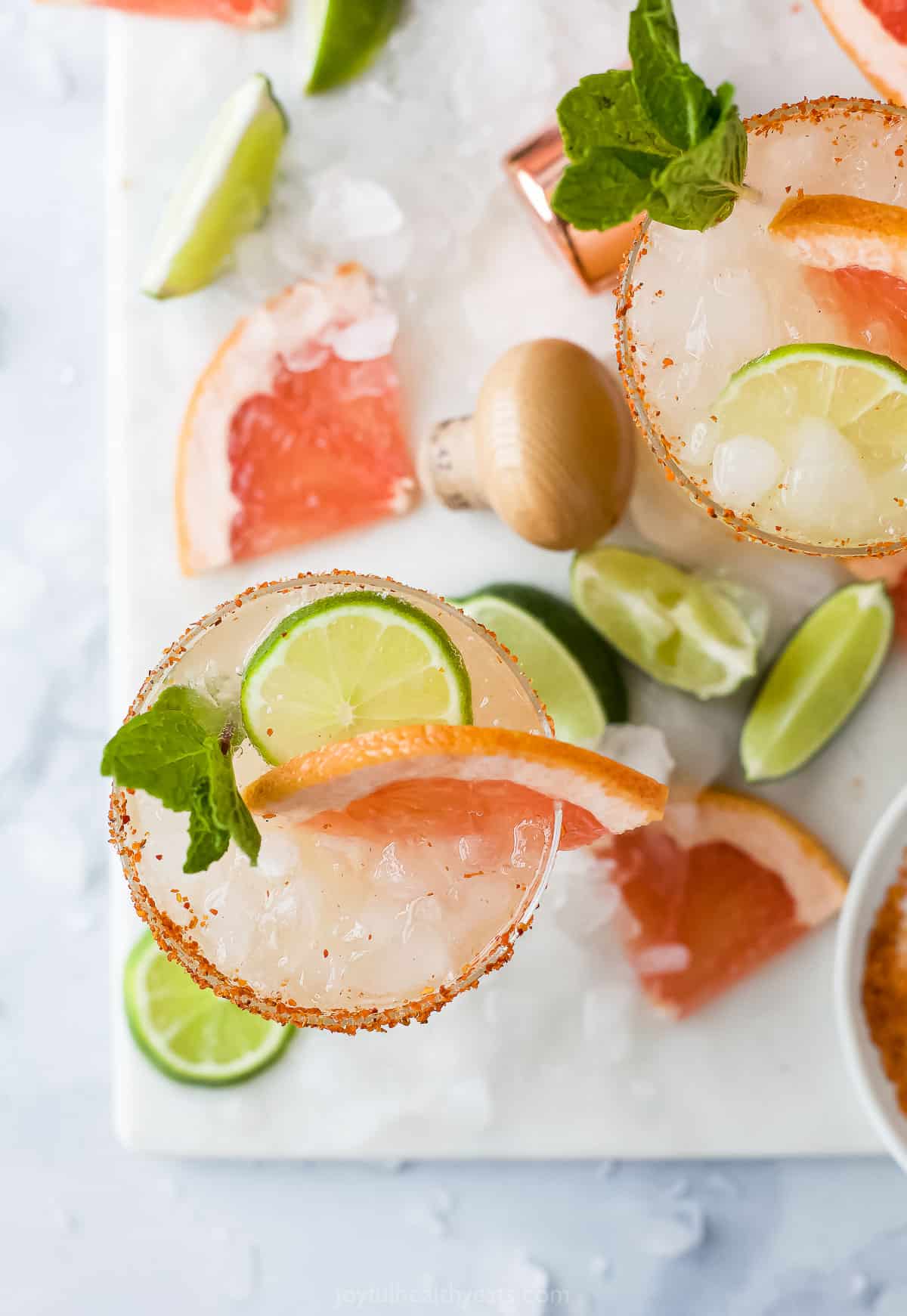 A Paloma cocktail garnished with a grapefruit wedge, a slice of lime and a sprig of mint