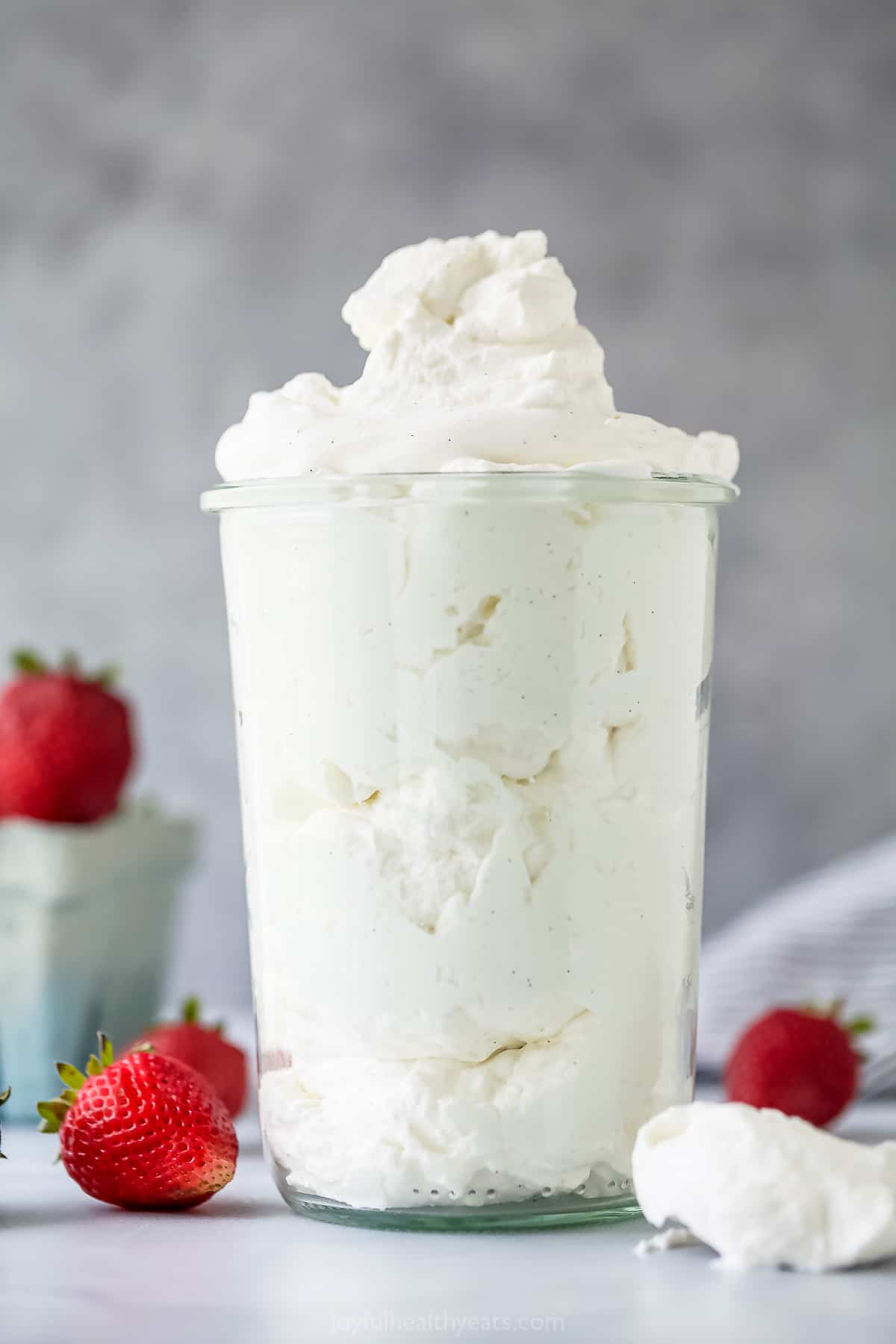 3 Ingredient Homemade Whipped Cream Recipe | Joyful Healthy Eats A large glass cup full of homemade whipped cream with fresh strawberries surrounding it