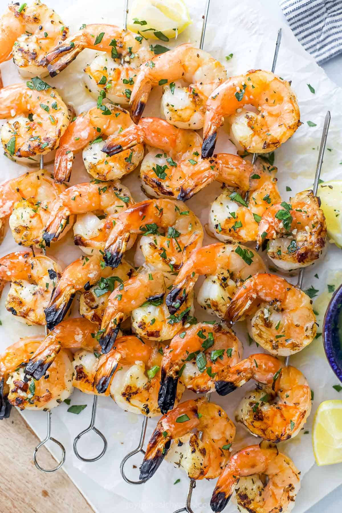 How to Grill Shrimp Perfectly Every Time | Joyful Healthy Eats Five grilled shrimp skewers on a sheet of parchment paper with fresh lemon wedges beside them