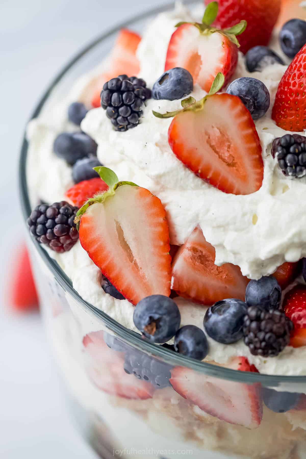 A close-up shot of the top of a strawberry shortcake trifle with a fresh strawberry in the background