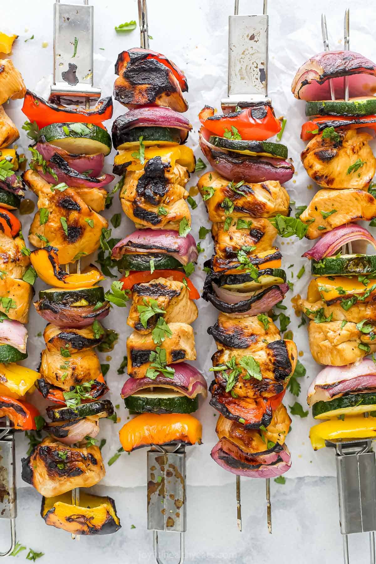 Tender chunks of chicken are soaked in a tangy, smoky marinade, then threaded onto skewers with fresh veggies in these flavorful kabobs! Grilled chicken kabobs on a sheet of parchment paper with chopped herbs sprinkled on top