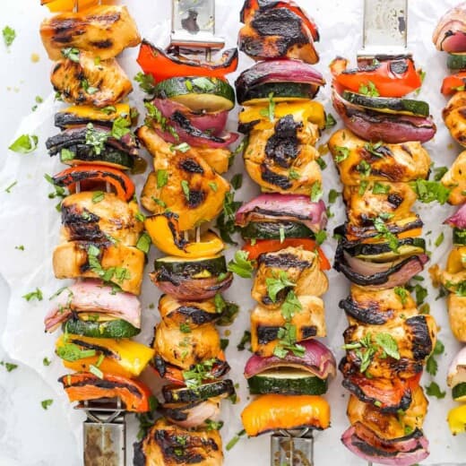 Four grilled chicken kabobs lined up on a countertop with a fifth one partially in frame