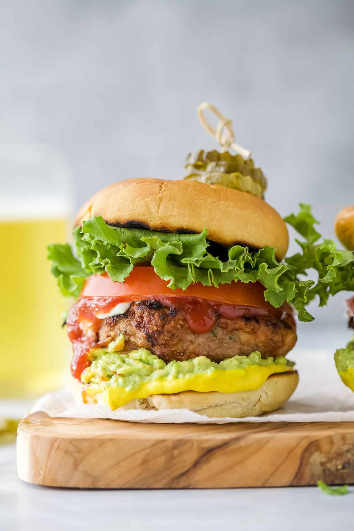 Tender, juicy and flavorful homemade turkey patties are seared to perfection on the grill and built into burgers with your favorite fixings! A homemade burger on a wooden cutting board with a glass of beer behind it