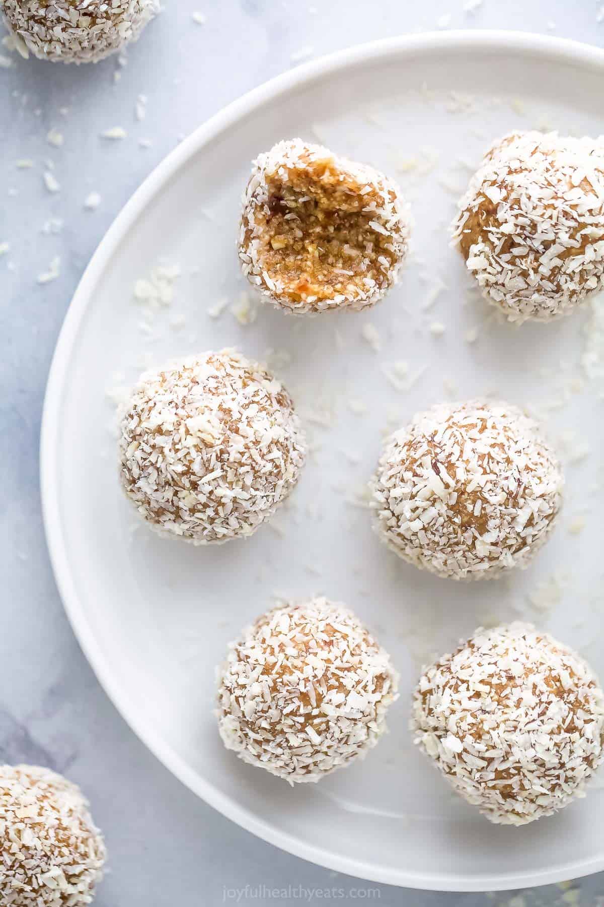 These Coconut Bliss Balls contain a boost of protein and a burst of sweet, nutty goodness. One batch will have you snacking happy all week! Coconut protein bites on a white plate with a raised rim