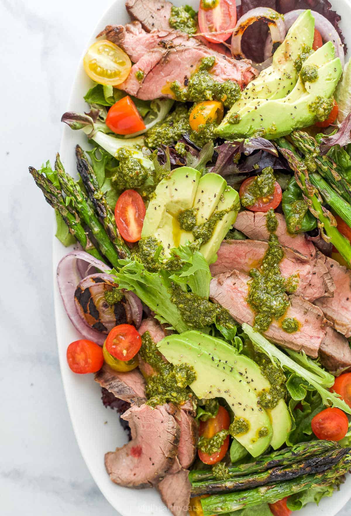 Served with chimichurri dressing, this grilled steak salad is fresh, light, flavorful and packed with protein! Plus, it's super easy to make. A platter of California steak salad topped with a drizzle of chimichurri dressing