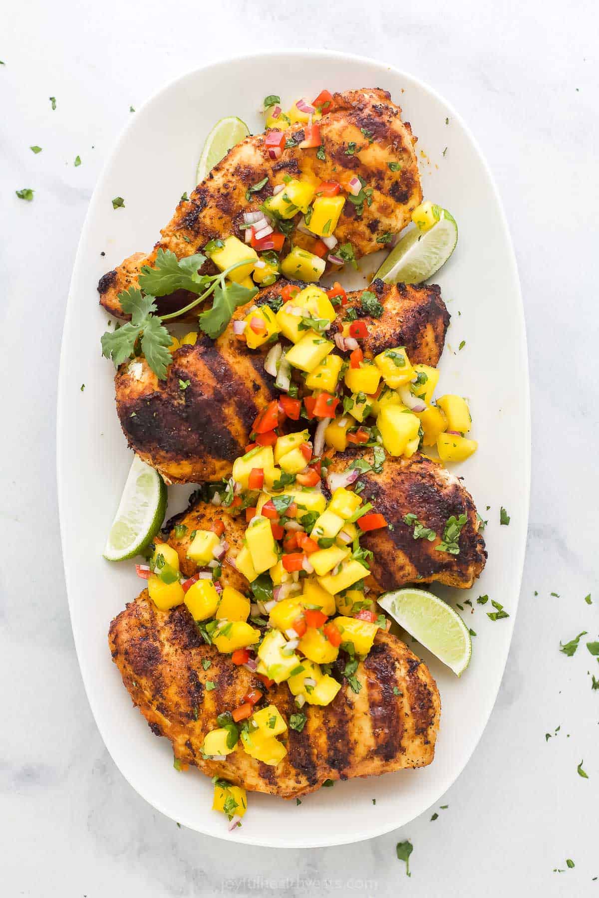 Tender chicken breasts are seasoned with a smoky, citrusy spice blend, then seared on the grill and smothered in sweet and spicy mango salsa! A platter full of mango chicken on a marble kitchen countertop
