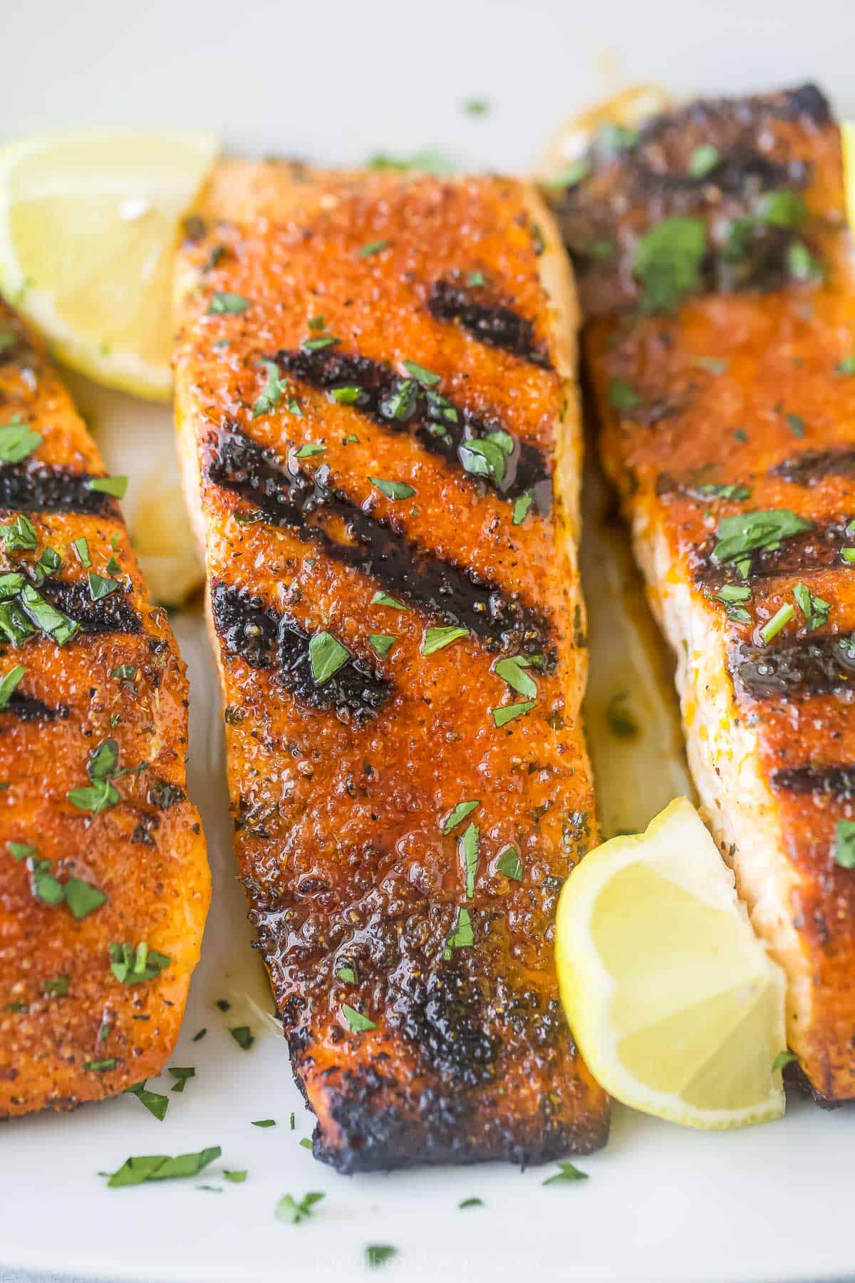 Grilled honey blackened salmon is crispy on the outside, moist and flaky on the inside, and loaded with classic Cajun flavor in every bite! A close-up shot of three blackened salmon fillets on a plate with fresh lemon wedges.