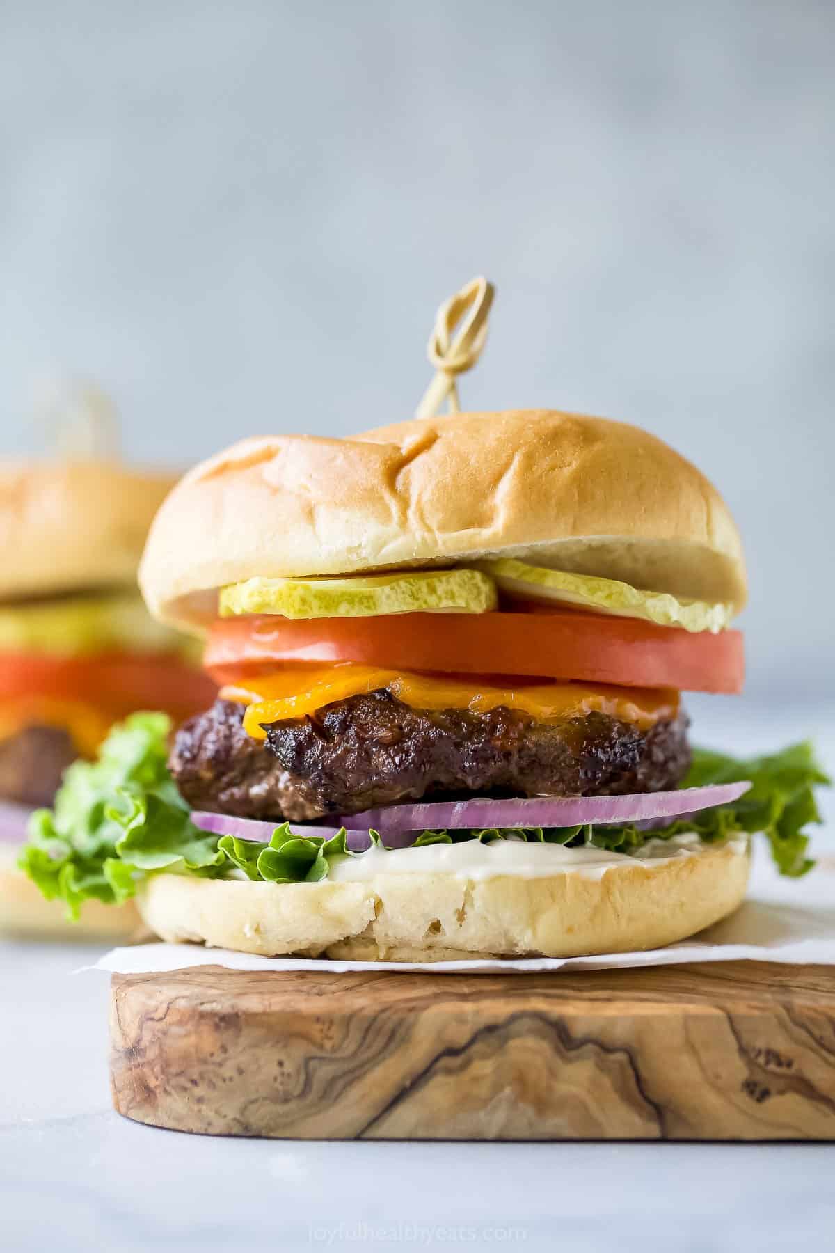 Here's how to cook the juiciest burger in the most simple way - the air fryer! Using an air fryer eliminates a greasy mess in the kitchen. Hamburger with cheese, lettuce, tomato, onion, and pickle on a cutting board