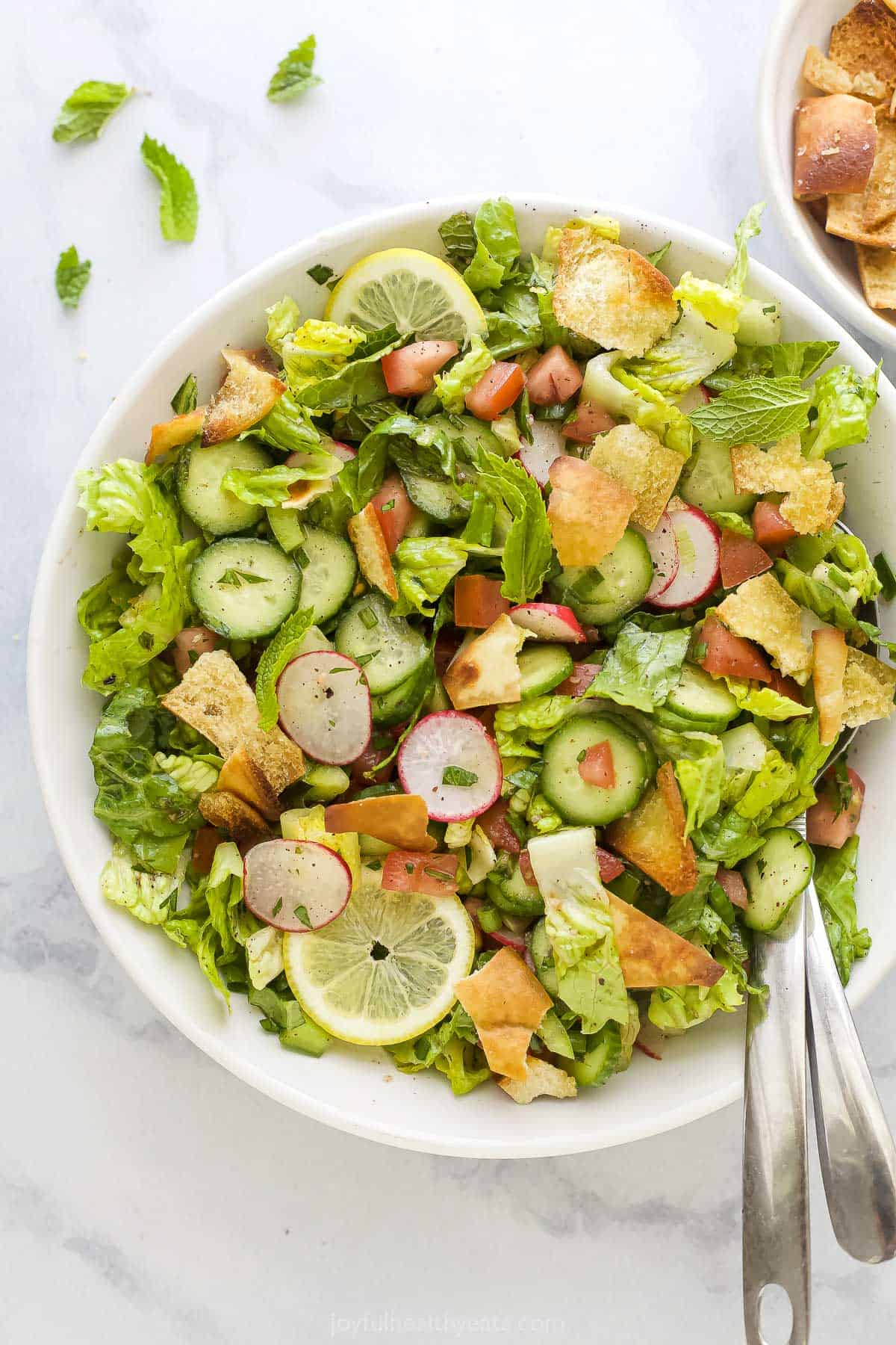 This easy Fattoush Salad features juicy tomatoes, crispy radishes, homemade pita croutons & more. It's finished off with a tangy vinaigrette! A Lebanese crouton salad on a kitchen countertop with a few bits of chopped parsley beside it