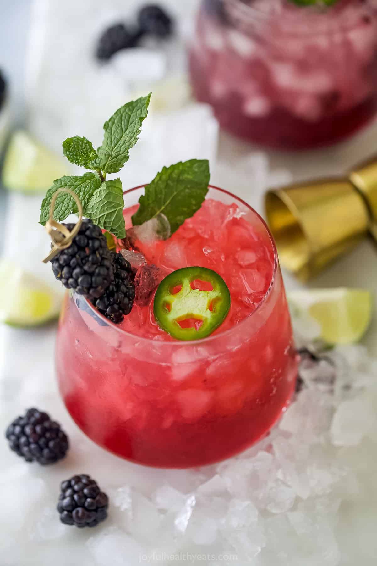Spicy jalapeño-infused tequila is combined with fresh lime juice, homemade blackberry simple syrup and more in this eye-catching margarita! A spicy blackberry margarita in a short cocktail glass with fresh fruit surrounding it