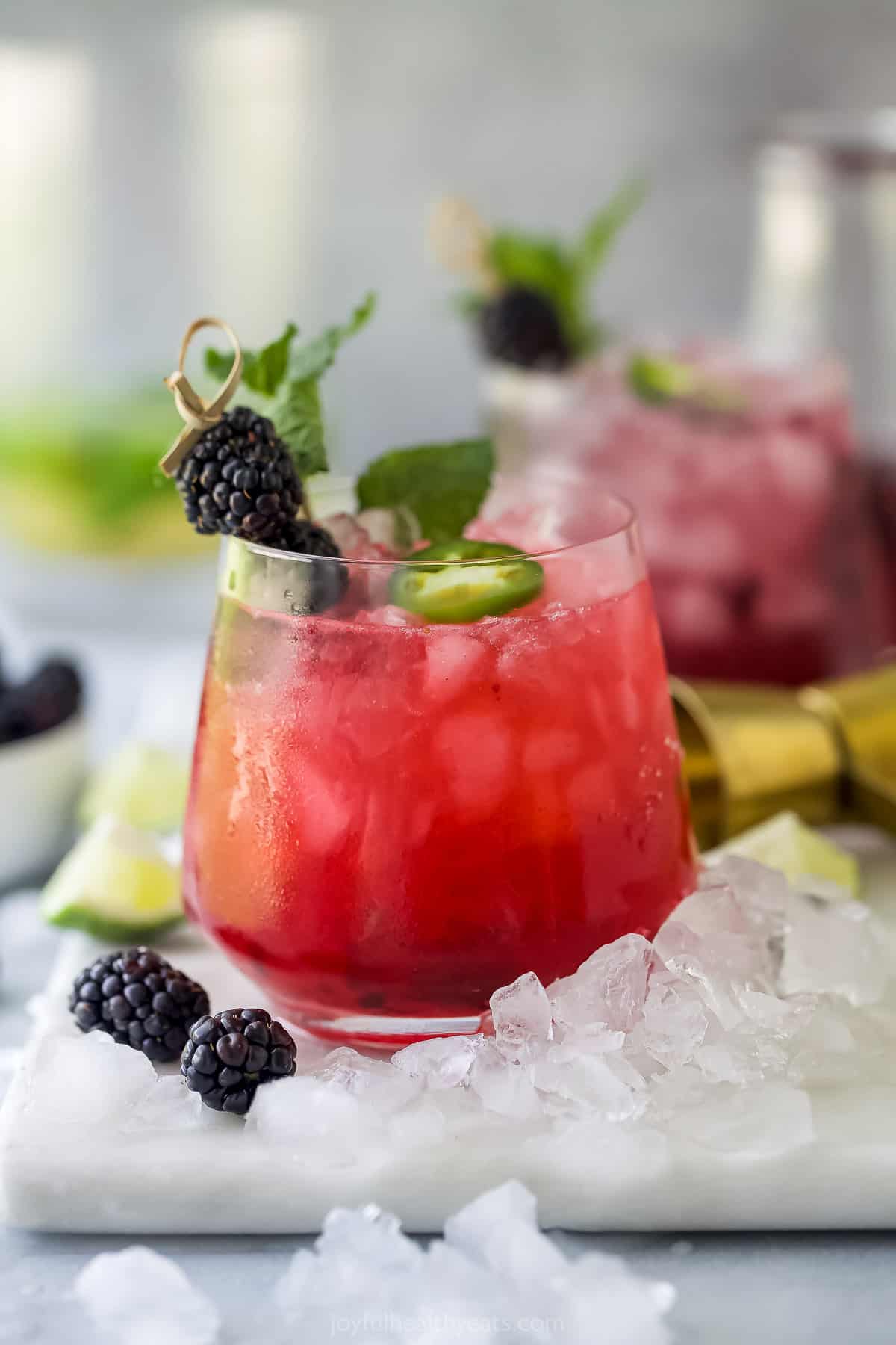 A blackberry jalapeño cocktail on a plastic cutting board with another one behind it