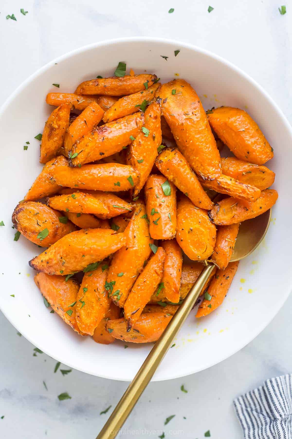 These easy Air Fryer Roasted Carrots are ready in under 15 minutes. Just season and go! The carrots are cooked perfectly every time. roasted and seasoned carrots in a white bowl with a gold spoon