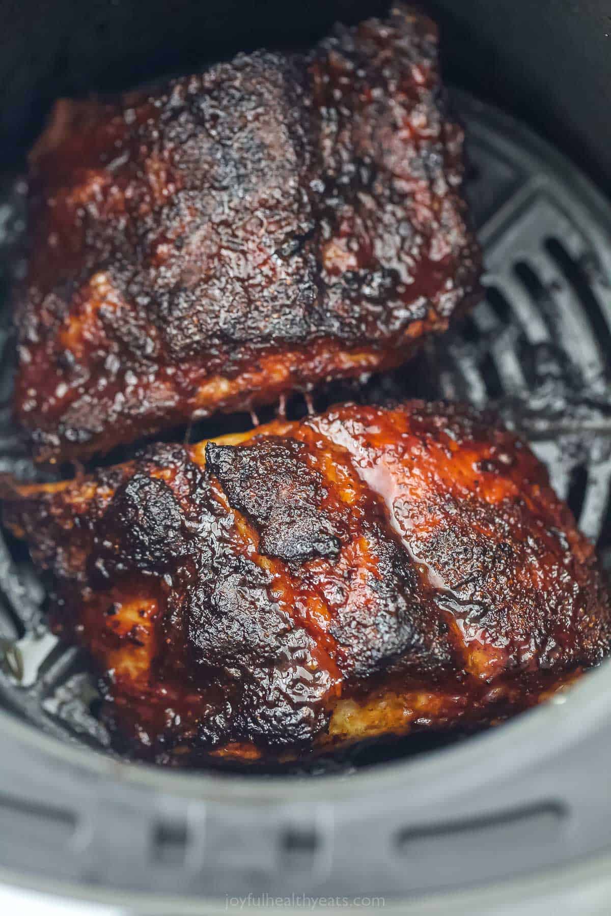 These Air Fryer Ribs taste like they're right off the BBQ. The ribs are tender and perfectly seasoned with a homemade spice rub and sauce. a close up of cooked BBQ ribs