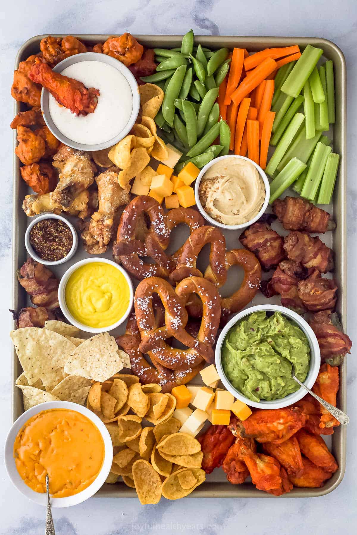 Here are some of my top Game Day Appetizers and Cocktails. It has everything from mocktails and margaritas to dips and wings! an assortment of snack foods on a tray like pretzels, chicken wings, cheese, veggie sticks, and tortilla chips scattered around dips like guacamole, mustard, and ranch
