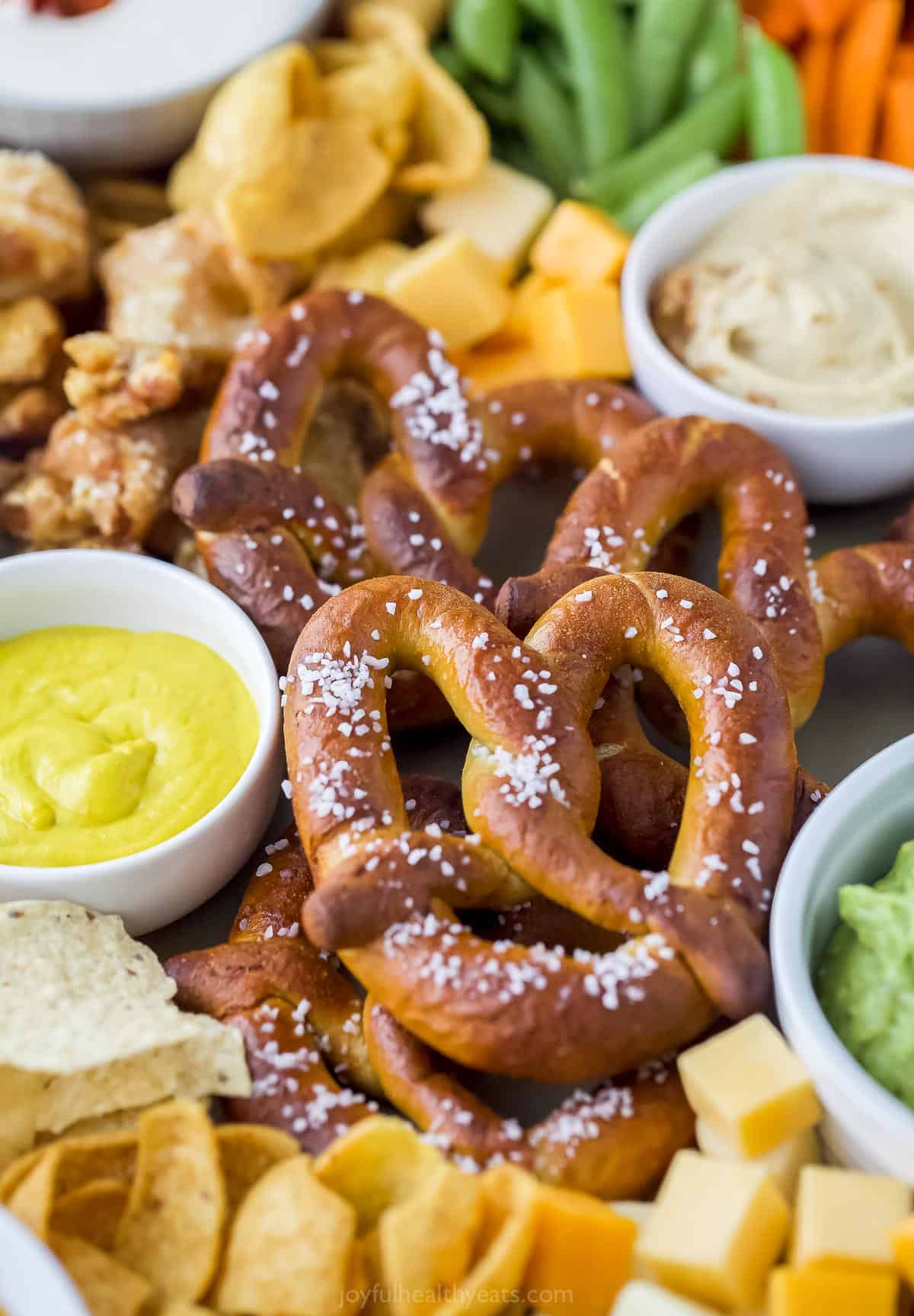 This Game Day Charcuterie Board is the snack recipe of the season! There's something for everyone from wings to guacamole to salty pretzels. a close up of preztels on a food tray with an assortment of other dips and snacks