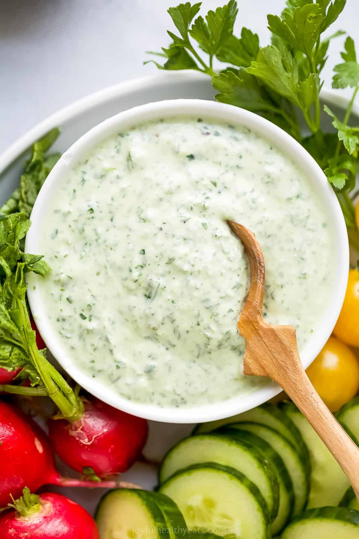 Whether you drizzle it over a salad or use it as a dip, you won't be able to get enough of this light and creamy Green Goddess Dressing. A bowl full of green goddess dressing with a small wooden spoon dipped inside